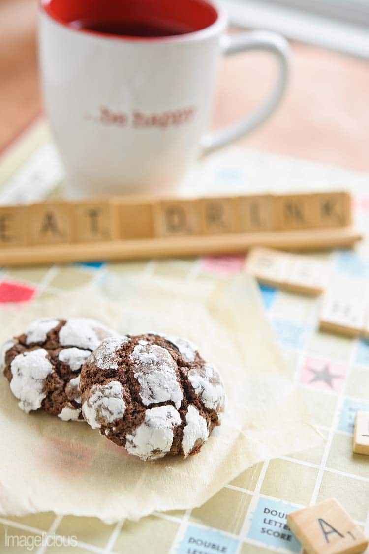 Close up of Chocolate-Mint Crackle Cookies on a scrabble board. Words "Eat drink" are visible in the background. Cup is in the background