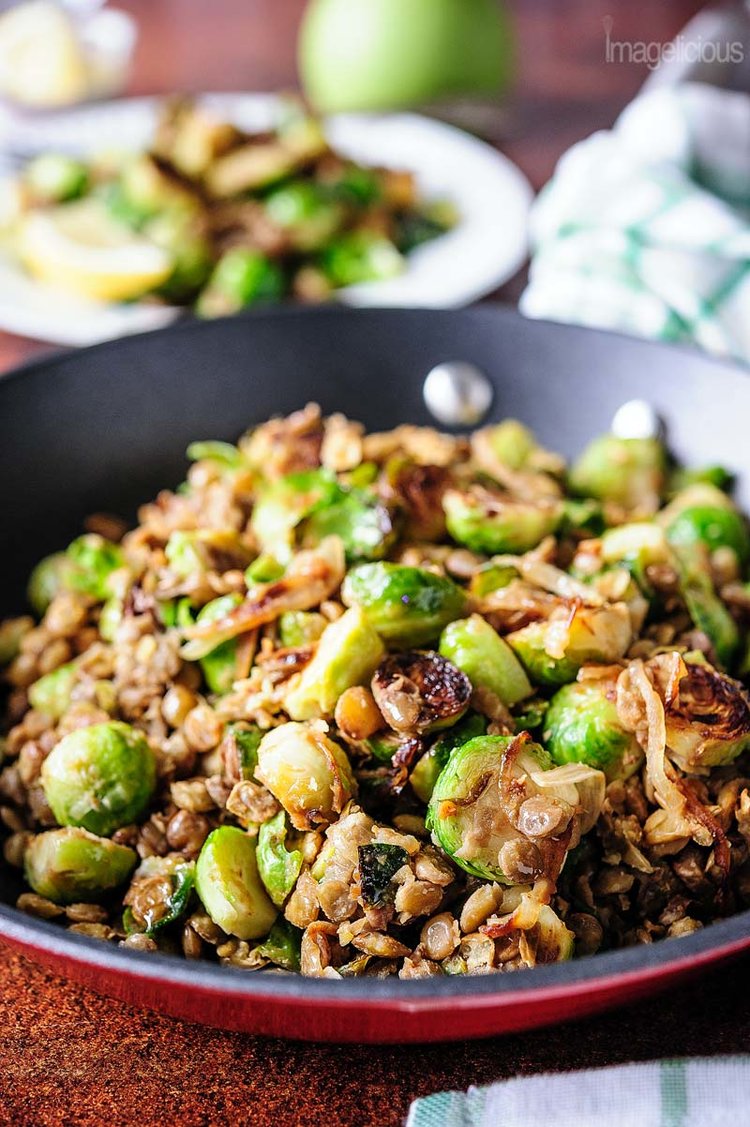 Photo of a skillet with Lentils and Brussels sprouts. A plate with more Brussels sprouts and lentils in the background