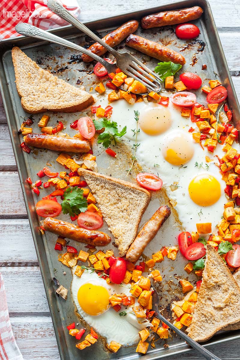 Sheet Pan with full breakfast of eggs, sweet potato hash, breakfast sausages, and bread with a few forks on the pan