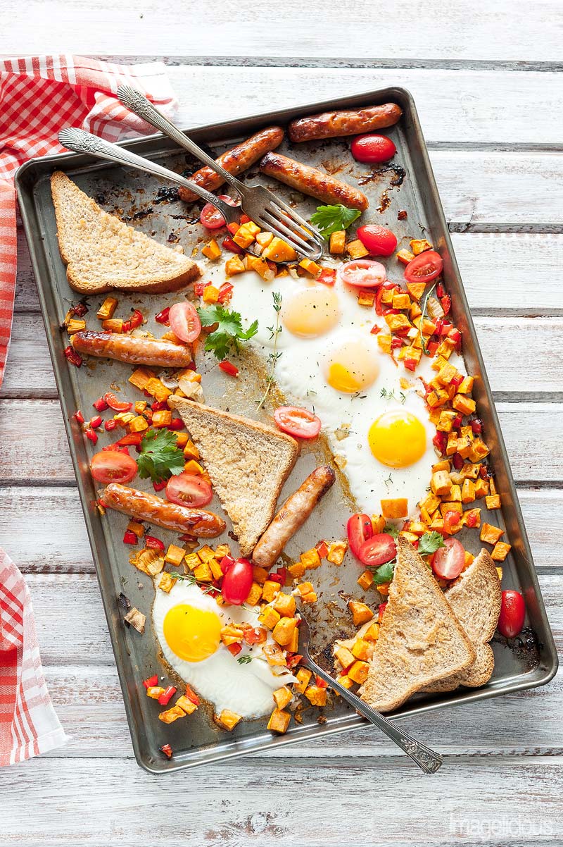 Top down view of a sheet pan with cooked full breakfast of eggs, sweet potato hash, sausages, and toasts