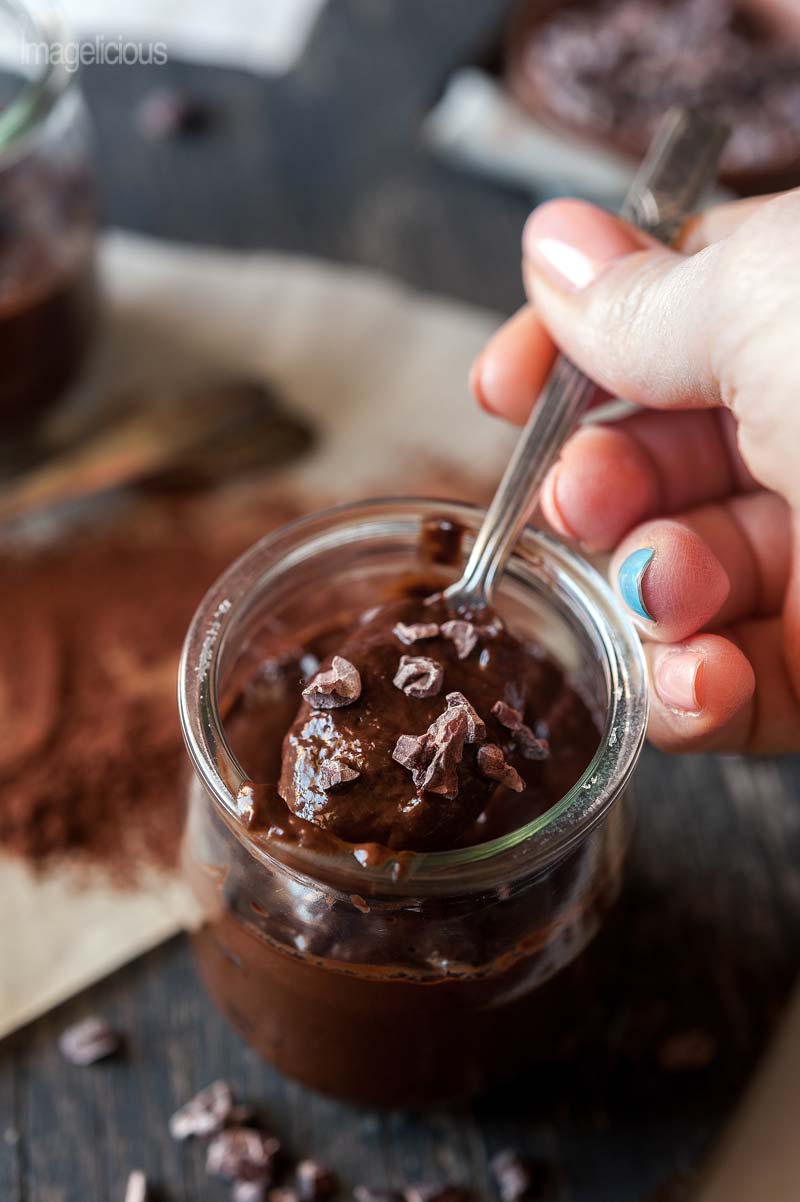 Closeup of a jar of Avocado Chocolate Pudding with a hand holding a spoon with the pudding