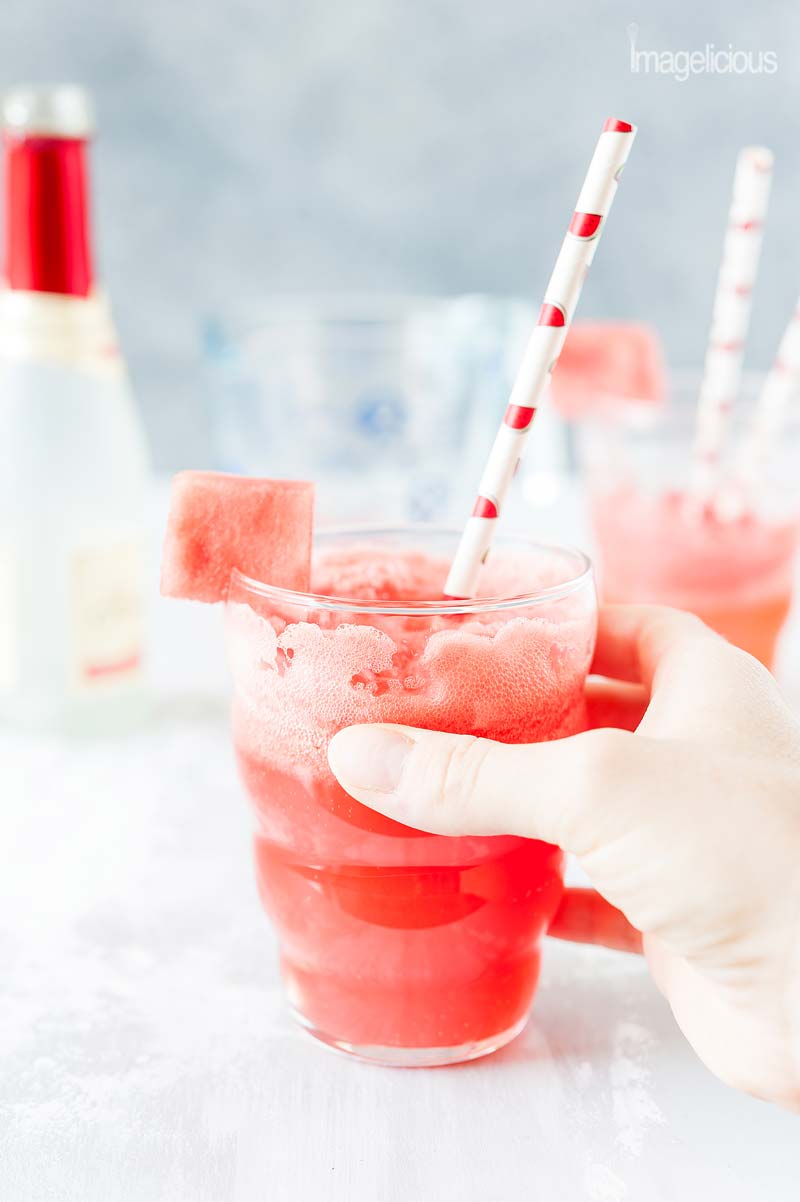 Closeup of a hand holding a glass of refreshing watermelon mimosa.