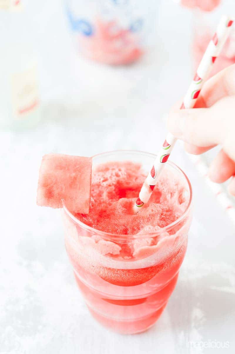 Closeup of a glass with Refreshing Watermelon Mimosa and a hand holding a straw in the glass.