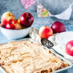 Sheet pan with Apple Meringue Tart in the forefront of the photo. A bowl with apples in the background. A few more apples around it. A stack of plates, napkin, and a cake server in the background.