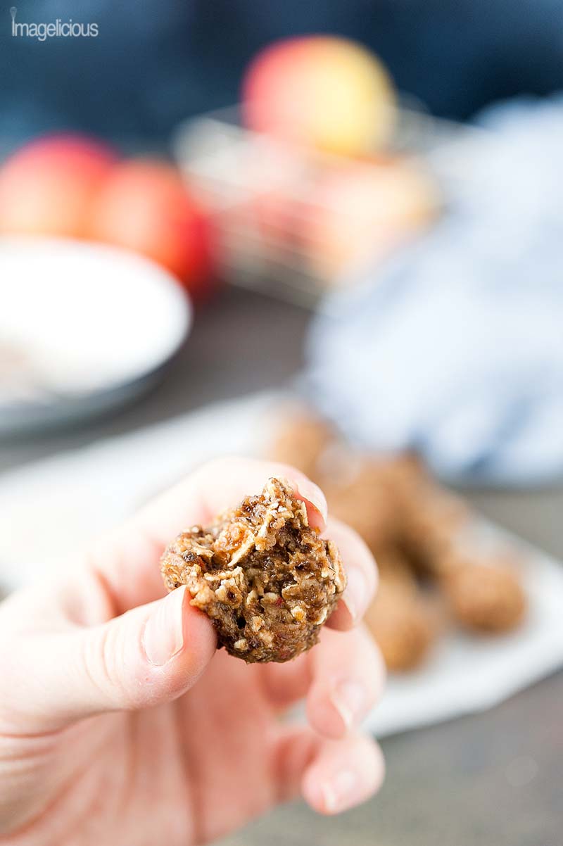 Closeup of a hand holding half of the Apple Pie Energy Ball. Few very blurred apples are visible in the background