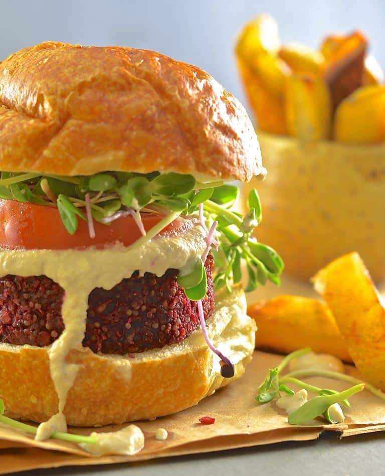 Close up of a fully loaded beet burger with fries in the background