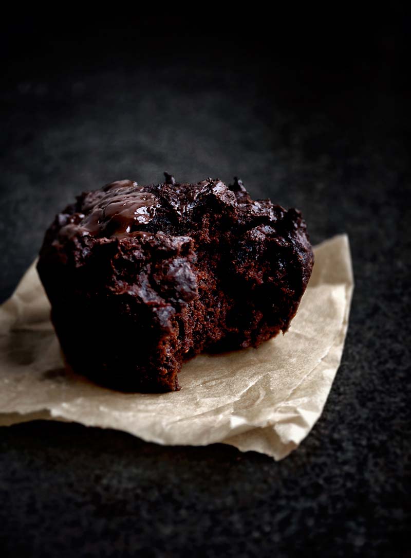Dark and moody photo of one chocolate beet muffin on a parchment paper