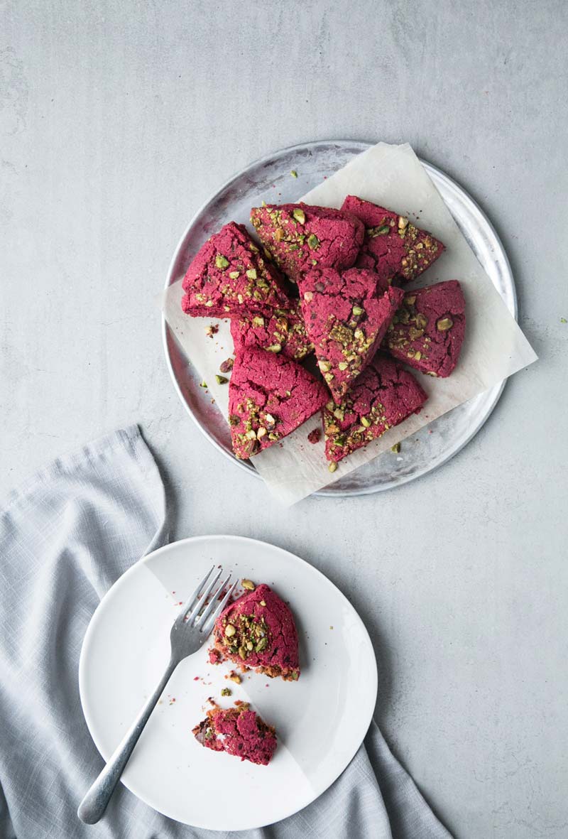 Top down view of a plate of pink triangular beet scones. A smaller plate is next to the platter with one scone half eaten