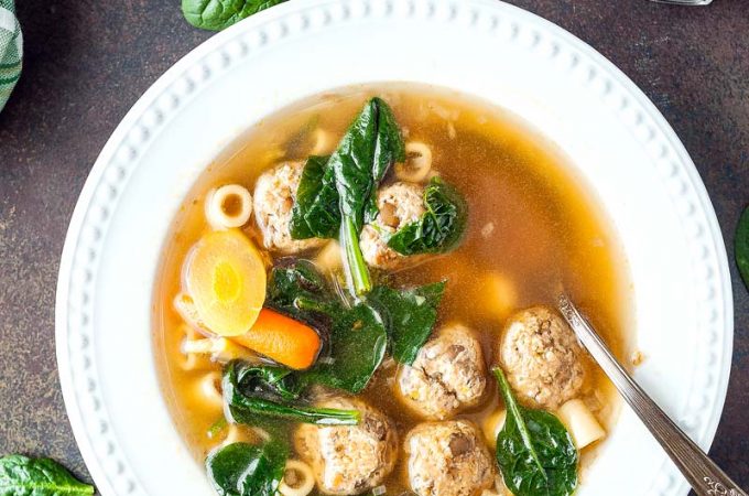 Top down view of a bowl filled with Instant Pot Meatball and Pasta Soup with a few spinach leaves scattered around the bowl