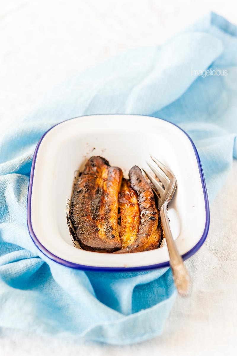 Small pan with deeply dark roasted bananas and a fork on blue napkin
