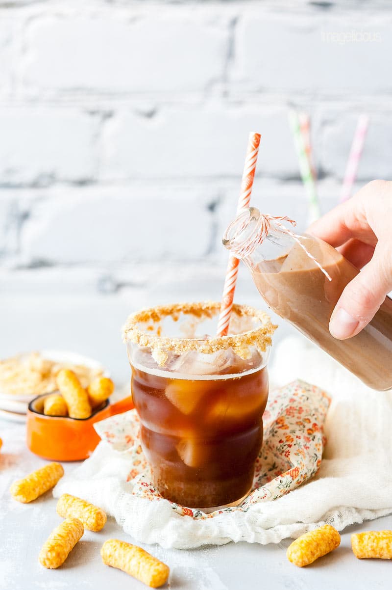Glass with Iced coffee and a peanut butter creamer that is just about to start being poured into the glass