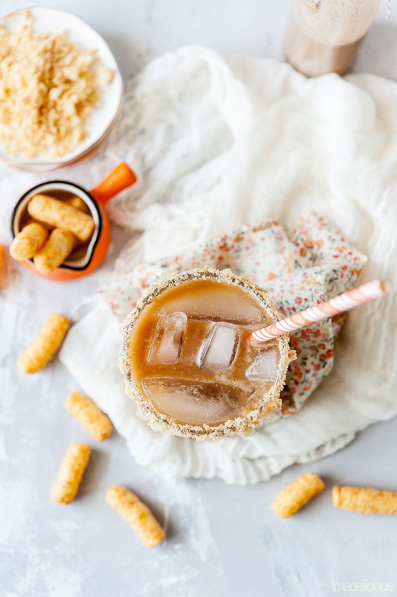 Top down view of a glass filled with Peanut Butter Iced Coffee and peanut butter puffs scattered around it