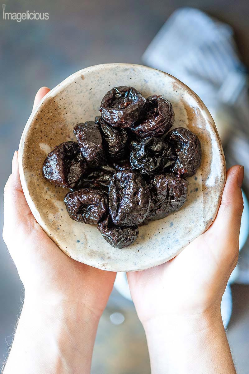 Close up of two hands holding a bowl with prunes