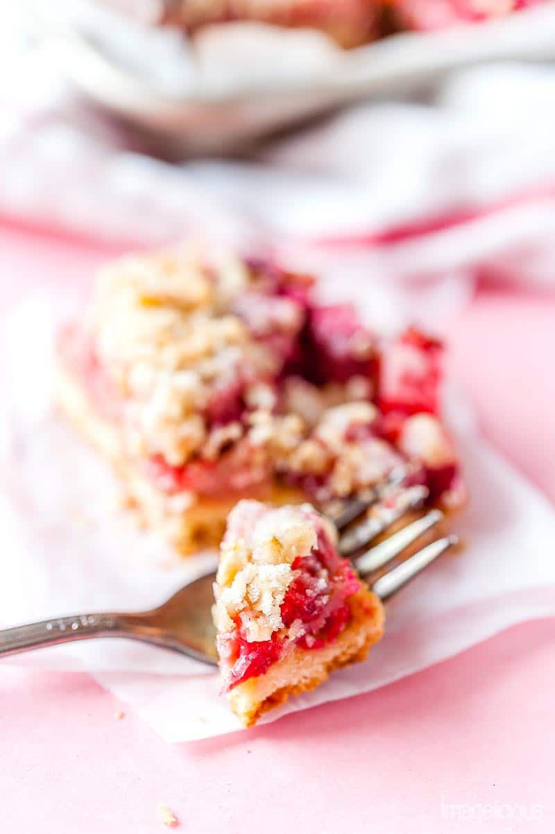 Closeup photo of a fork with a piece of Strawberry Rhubarb Bar and a bar behind it