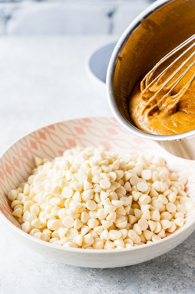 Pumpkin caramel is being poured over a bowl of white chocolate chips