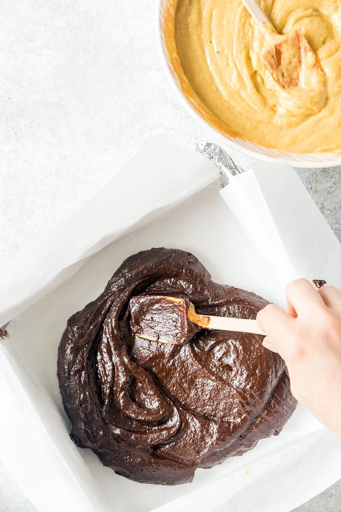 Process shot: dark fudge is being spread inside a baking form