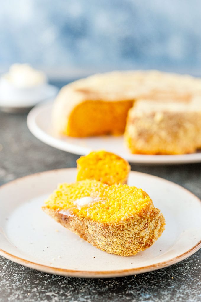 Photo os a slice of Instant Pot Cornbread with a bit of butter on top of it and the rest of the cornbread in the background