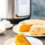 Slice of Instant Pot Cornbread with the rest of the cornbread in the background and an Instant Pot behind it
