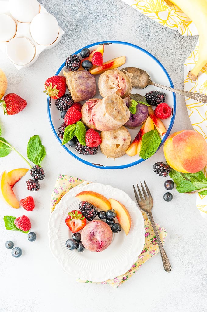 Top down photo of a plate full of Instant Pot Fruity Egg Bites and a small dessert plate with just one Instant Pot Fruity Egg Bite. Lots of fruits and berries around the egg bites