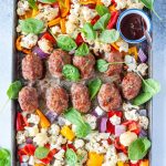 Sheet Pan Mini Meatloaves with Vegetables and spinach around them, also a small ramekin of extra bbq sauce
