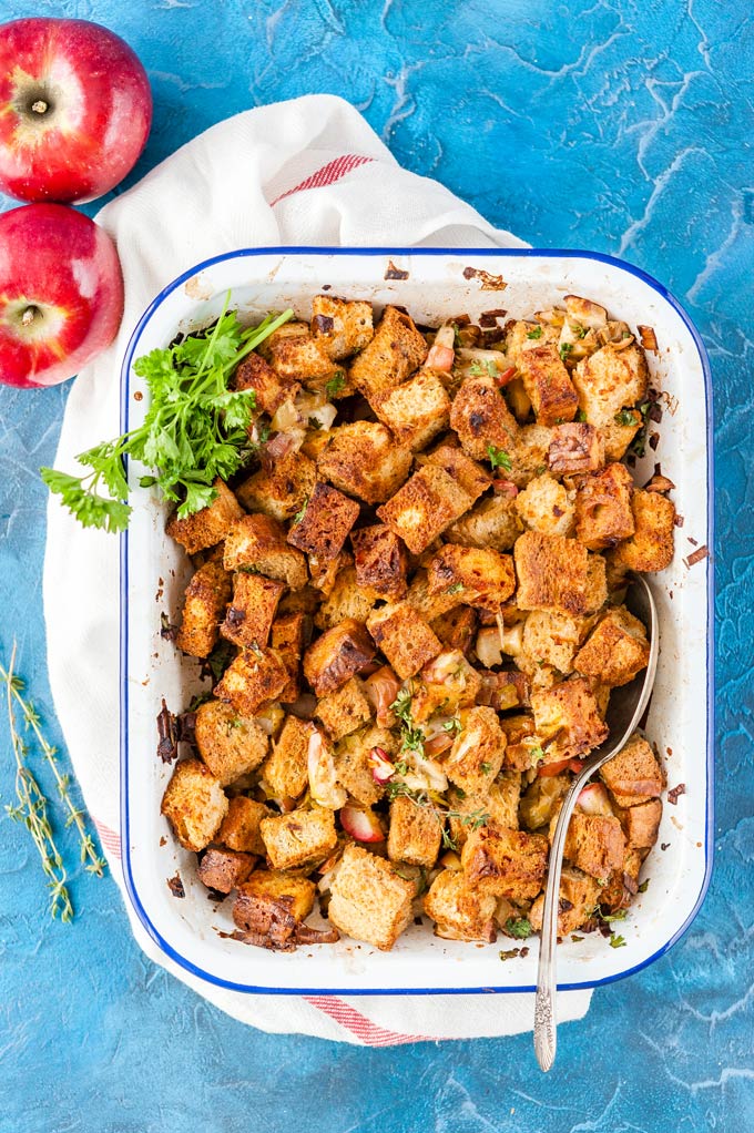 Baked Cornbread and Apple Stuffing in a pan with a spoon and a few whole apples on the side
