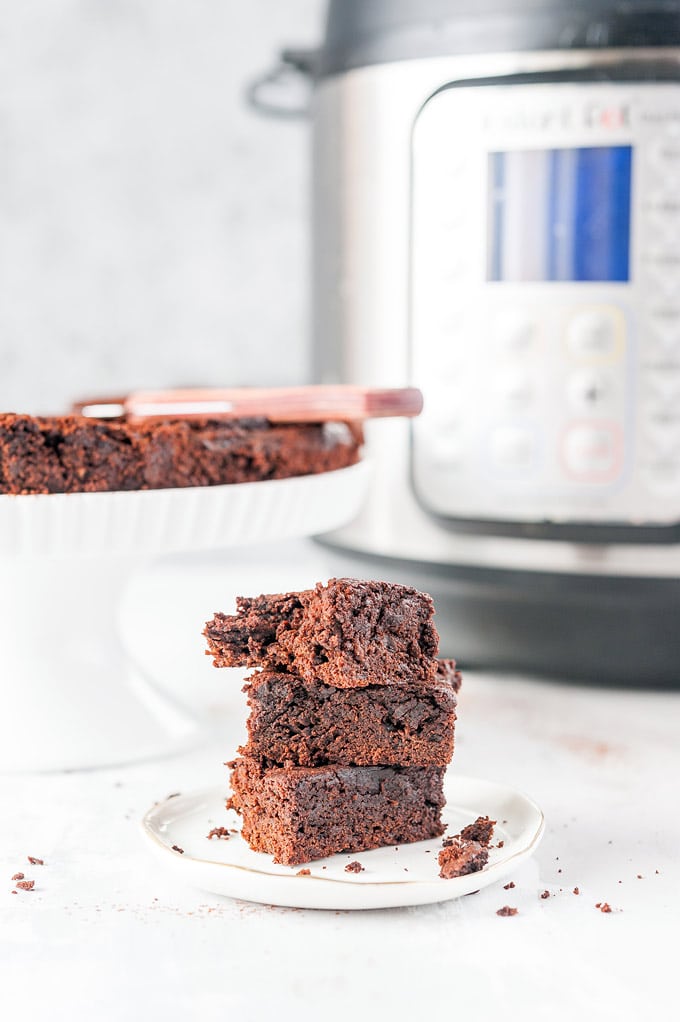 A stack of three Instant Pot Brownies with a cake plate with the rest of the brownies and an Instant Pot in the background