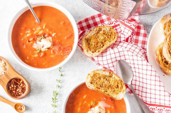 Top down view of two bowls of Instant Pot Tomato Orzo Soup with a few garlic toasts around and Instant Pot with the rest of the soup on the side