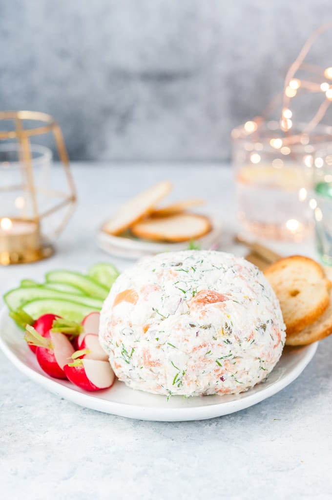 Whole round Smoked Salmon Cheese Ball on a plate with radishes, cucumbers, and crackers