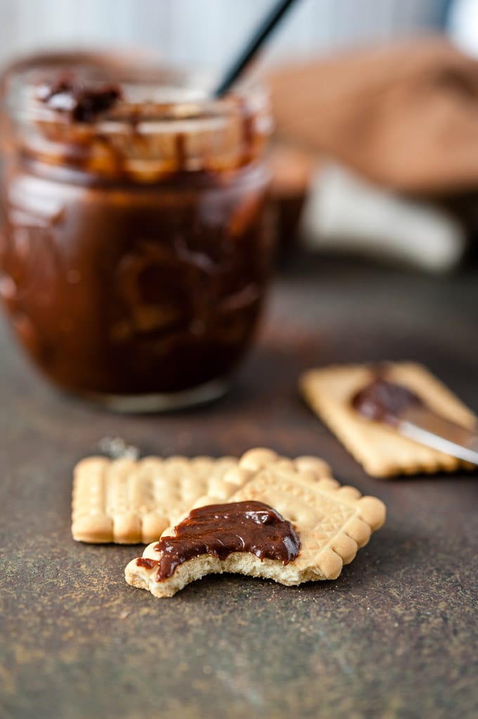 A little bit of Chocolate Caramel Sauce is spread on a half eaten cookie. A jar of sauce is in the background