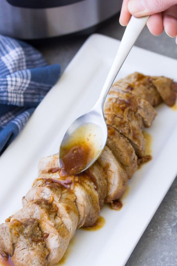 Sliced pork tenderloin on a plate with a spoon drizzling sauce over it