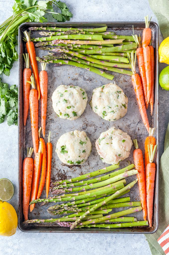 Sheet pan with raw asparagus, carrots, and fish cakes before being baked