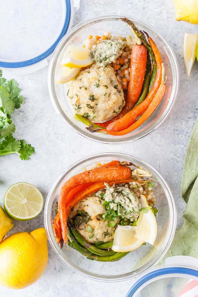 Closeup of meal prep containers with oven baked fish cakes, roasted carrots, asparagus, couscous and pesto