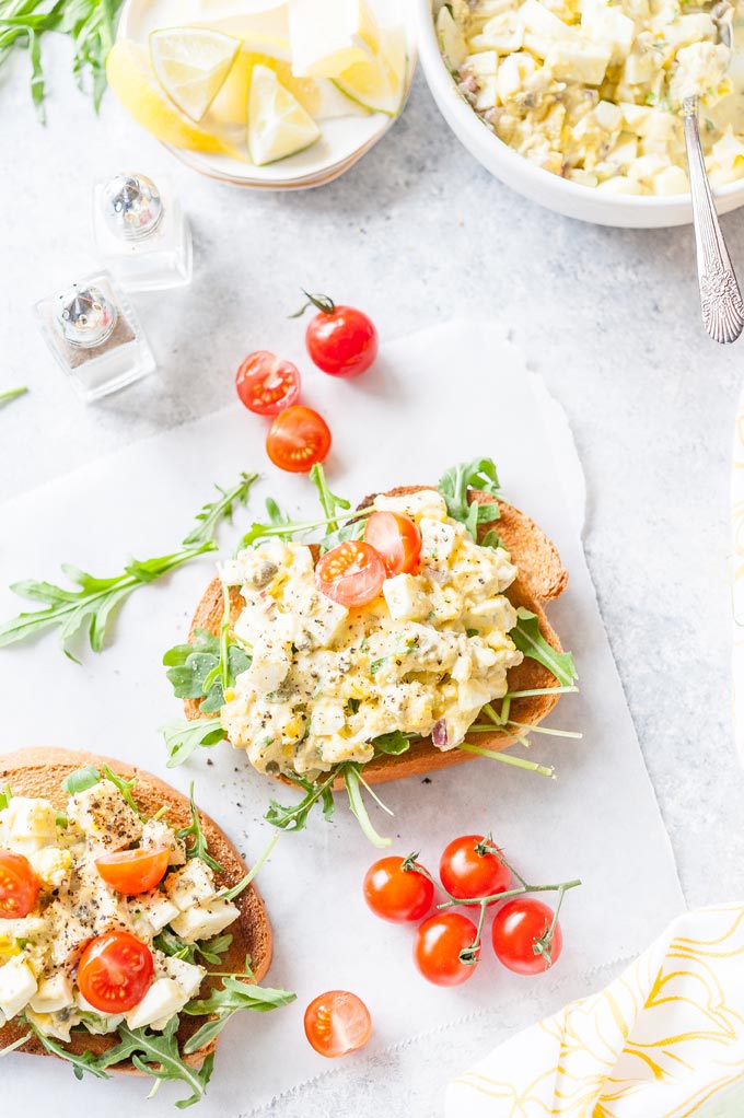 Two Tarragon Egg Salad open-faced Sandwiches with a bowl of extra salad in the corner
