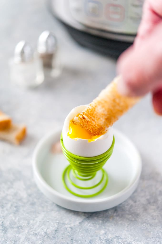 Hand dipping a slice of toast into a soft boiled egg.