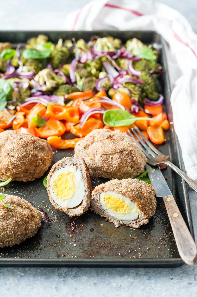 Cut up Baked scotch egg on a sheet pan with vegetables.