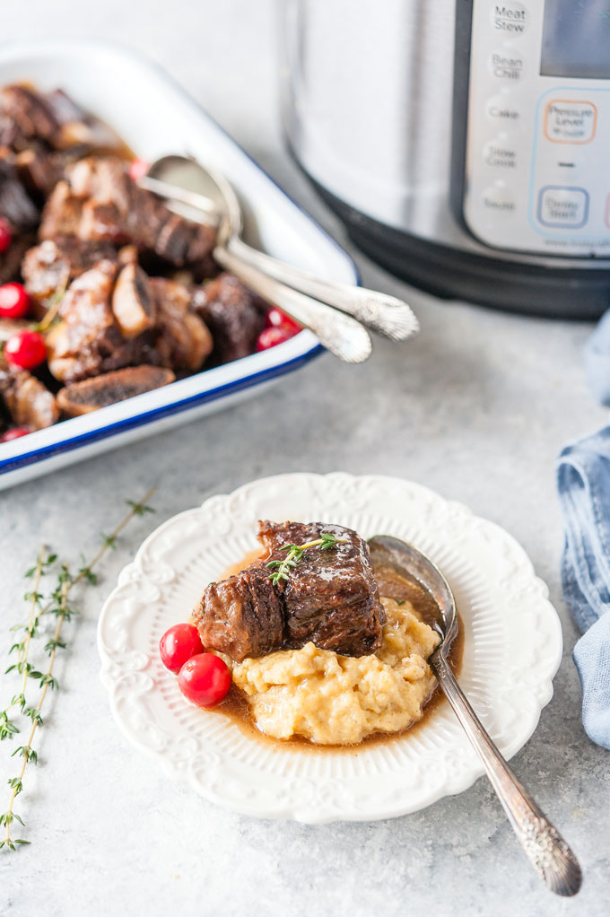 Plate with beef short ribs over creamy polenta and Instant Pot in the background.