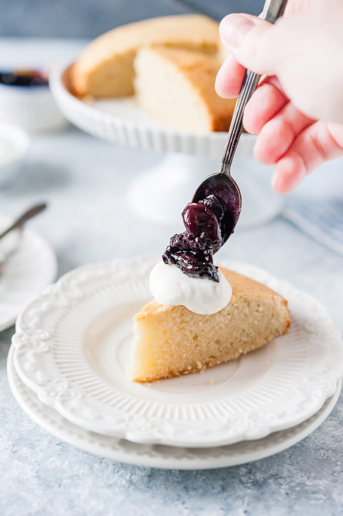 Hand drizzling some berry sauce over a slice of almond cake.