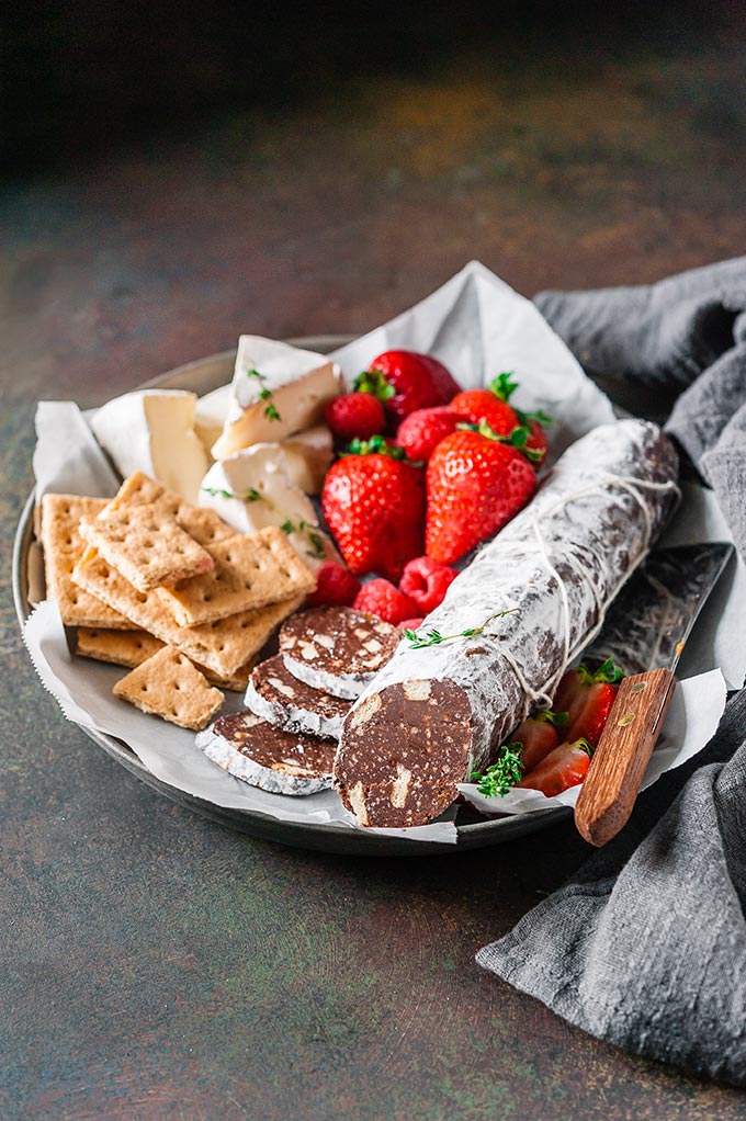 Plate with chocolate salami, crackers, cheese, and strawberries.